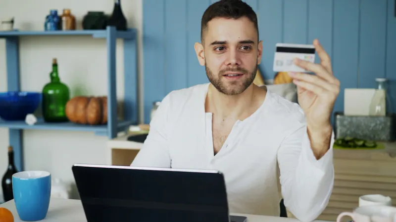 Person holding a payment card while shopping online with a laptop.
